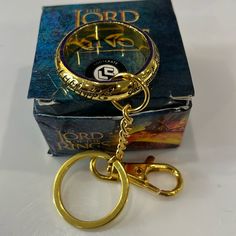 a golden keychain sitting in front of a box with a ring on it