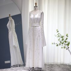 a white dress is on display in front of a mirror and vase with some flowers