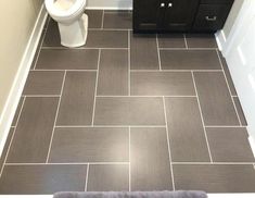 a white toilet sitting in a bathroom next to a brown cabinet and counter with a gray rug on the floor