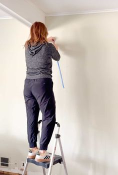 a woman standing on a ladder painting the wall