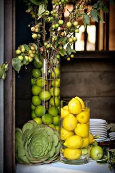 a vase filled with lots of yellow lemons next to a pile of green apples