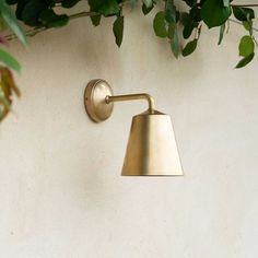 a brass wall light on a white wall with green leaves hanging from it's side