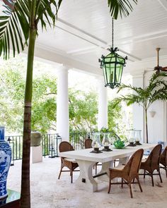 an outdoor dining area with wicker chairs and table surrounded by potted plants on the porch