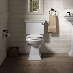 a white toilet sitting next to a sink in a bathroom under a window with a towel hanging on it