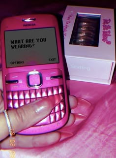 a pink cell phone sitting on top of a bed next to a box with the message what are you wearing?