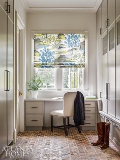 a white chair sitting in front of a window next to a desk and cupboards