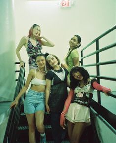 four girls are standing on an escalator and posing for the camera