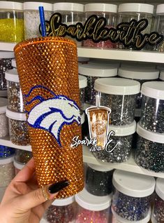 a hand holding a sparkle tumbler in front of some glitters and other items