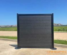 a large black gate sitting on the side of a road next to an empty field