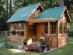 a small wooden shed with green roof and flowers on the front lawn in front of it