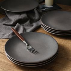 a stack of black plates with a wooden fork on top of them next to a glass of milk