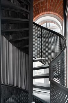 a spiral staircase in front of a brick wall and window with white curtains on it