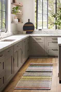 a kitchen with gray cabinets and white counter tops, wooden flooring and an area rug in front of the window