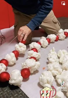 a man is decorating some food on a table with red and white balls in the shape of popcorn