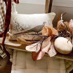 a bird sitting on top of a pillow next to some leaves and pumpkins in front of a window