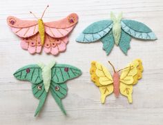 four felt butterflies sitting on top of a wooden table next to each other and one butterfly has its wings folded