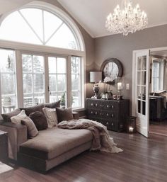 a living room filled with furniture and a chandelier hanging from the ceiling next to a large window