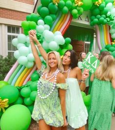 two beautiful women standing next to each other in front of a balloon arch with green balloons