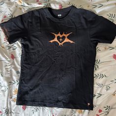 a black t - shirt with an orange design on the chest and two hearts in the middle