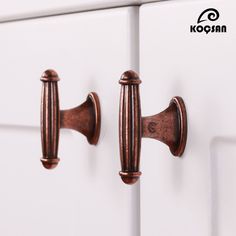 two door handles on the side of a white cabinet with copper hardware and knobs