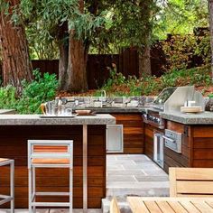 an outdoor kitchen with bar stools next to it and trees in the back ground