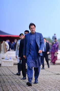 a man in a blue suit and tie walking down the street with other people behind him