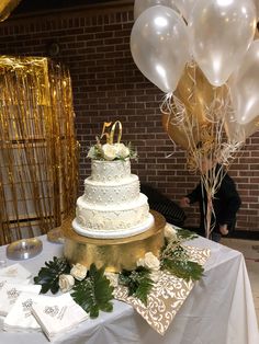 a white wedding cake sitting on top of a table next to balloons and greenery