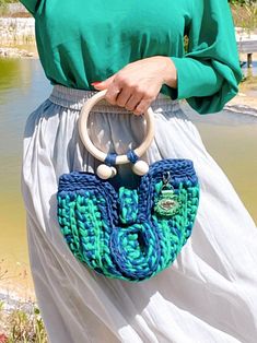 a woman holding a blue and green purse over her shoulder in front of a body of water