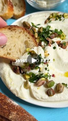 a person holding a piece of bread over a bowl of hummus and olives