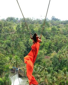 a woman in an orange dress is swinging from a rope over a river surrounded by palm trees