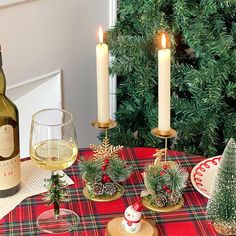 a table set for christmas with wine, candles and pine cones on the placemat