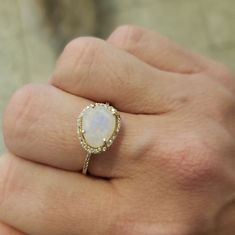 a woman's hand holding a ring with a white stone in the middle and diamonds around it