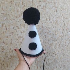 a hand holding a white and black party hat with pom - poms on it