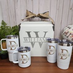 a set of three white coffee mugs sitting on top of a wooden table next to a cooler