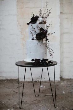 a three tiered white cake sitting on top of a black table next to a brick wall