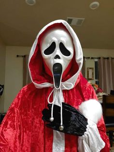 a person in a red robe with a white mask holding a black bag and tongue sticking out