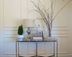 a glass table topped with a vase filled with flowers next to a lamp on top of a hard wood floor