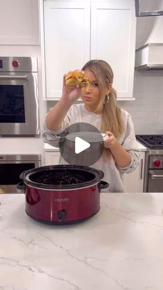 a woman standing in front of a crock pot with food in it and looking at the camera