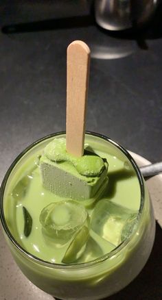 a green drink with ice cubes in it and a wooden stick sticking out of the top