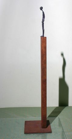 a small statue is standing on top of a wooden stand with a shadow cast on the wall behind it