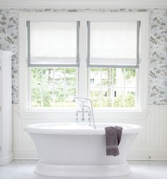 a white bath tub sitting next to two windows in a room with wall paper on the walls