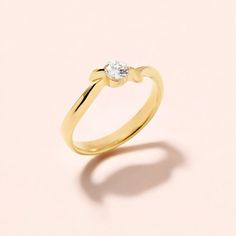 a yellow gold ring with a single diamond on the top, against a pink background