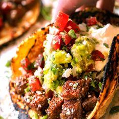 someone is holding up a taco with meat and vegetables on it, ready to be eaten