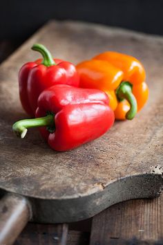 three peppers sitting on top of a wooden cutting board