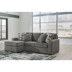 a living room with a gray sectional couch and rugs on the floor in front of large windows