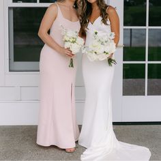 two beautiful women standing next to each other in front of a white door holding bouquets