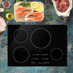 an electric cooktop with meat, fish and vegetables on the counter next to it