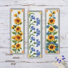 two cross stitch bookmarks with sunflowers and bluebells in them on a white wooden background