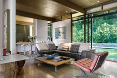 a living room filled with furniture next to a large glass window covered wall and wooden flooring