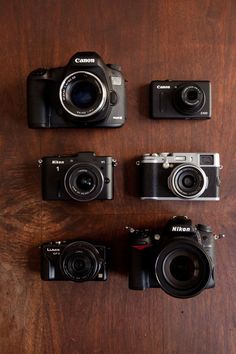 four cameras sitting on top of a wooden table